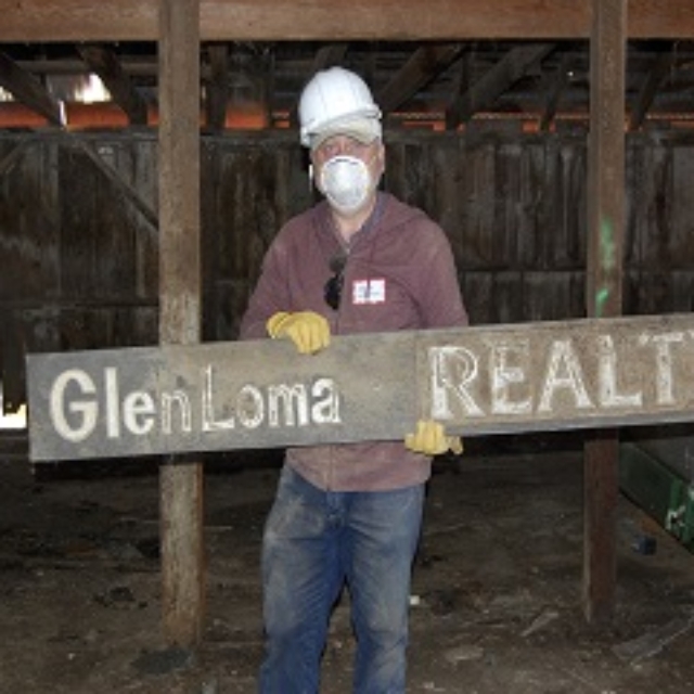 man,hard hat,gloves,sign,glenloma realty,barn,mask