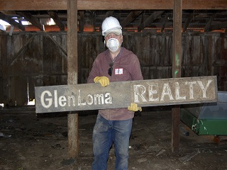 man,hard hat,gloves,sign,glenloma realty,barn,mask